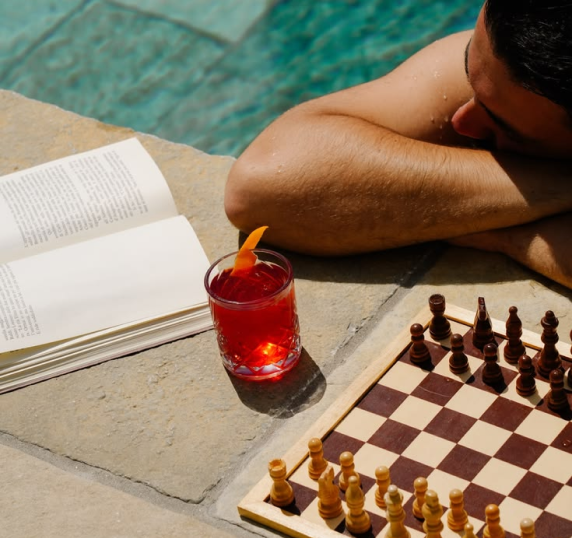 A poolside drink beside a chessboard and an open book